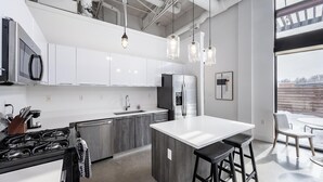 A modern kitchen with white cabinetry, stainless steel appliances, and a large island with bar stools. - Landing | Beautiful 1BD, Pool, Gym (Royal Oak)