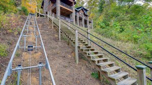Una scala in legno conduce a un edificio in pietra con un balcone, immerso in un paesaggio autunnale.