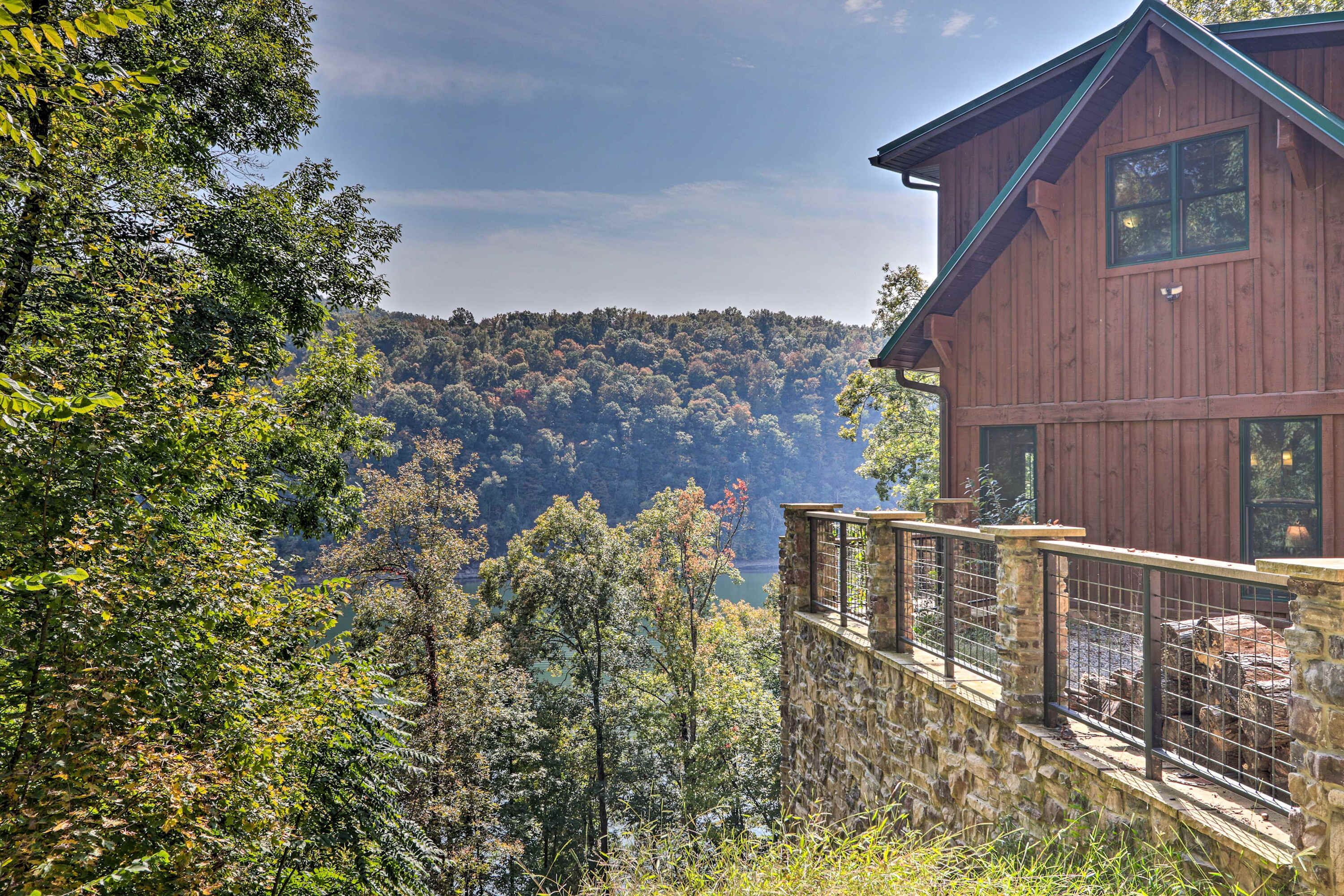 A wooden cabin with a stone foundation, surrounded by dense forest and overlooking a valley.