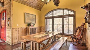 Un tavolo da pranzo in legno con panche, una porta rossa, un'ampia finestra ad arco e una testa di animale appesa al muro.