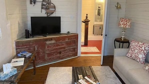 A living room with a TV, wooden walls, a sofa, a lamp, and a small table with books. - Salt box on Brinson’s (Winterton)