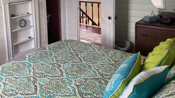 A bedroom with a patterned bedspread, a hanging light fixture, a dresser with a mirror, and a door leading to a balcony. - Salt box on Brinson’s (Winterton)