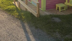 A small, single-story building with a red exterior and a yellow trim. It has a small window and a door, with a wooden deck in front. - Salt box on Brinson’s (Winterton)