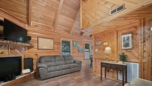 L’intérieur d’un chalet en bois, avec un canapé, un téléviseur, une cheminée et une table sur laquelle se trouve une lampe.
