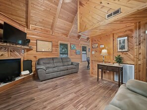 A wooden cabin interior with a sofa, a television, a fireplace, and a table with a lamp. - Near Dollywood Cabin Escape・Deck・Private Hot Tub (Gatlinburg)