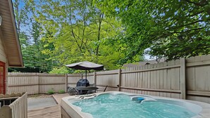 Un jardin avec un jacuzzi, une terrasse en bois, une table de patio et un parasol.