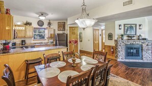 A spacious kitchen with wooden cabinets, a dining area with a large wooden table and chairs, and a stone fireplace. - Cozy 2BR Resort Condo Near Dollywood・Pools ・Sauna (Pigeon Forge)