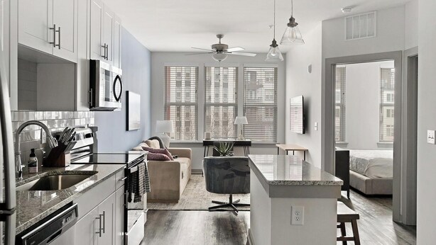 A modern kitchen with a dining area, a living room with a sofa and a TV, and large windows with blinds. - Landing | Stylish 1BD, Pool, Clubhouse (Nashville)
