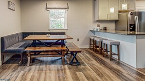 A modern kitchen with a built-in island, bar stools, and a dining area with a bench and table. - Lakefront Cabin, Sleeps 14・2 Level Dock・Sun Deck (LaFollette)