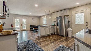 A modern kitchen with wooden flooring, a stainless steel refrigerator, and a dining area with a bench. - Lakefront Cabin, Sleeps 14・2 Level Dock・Sun Deck (LaFollette)