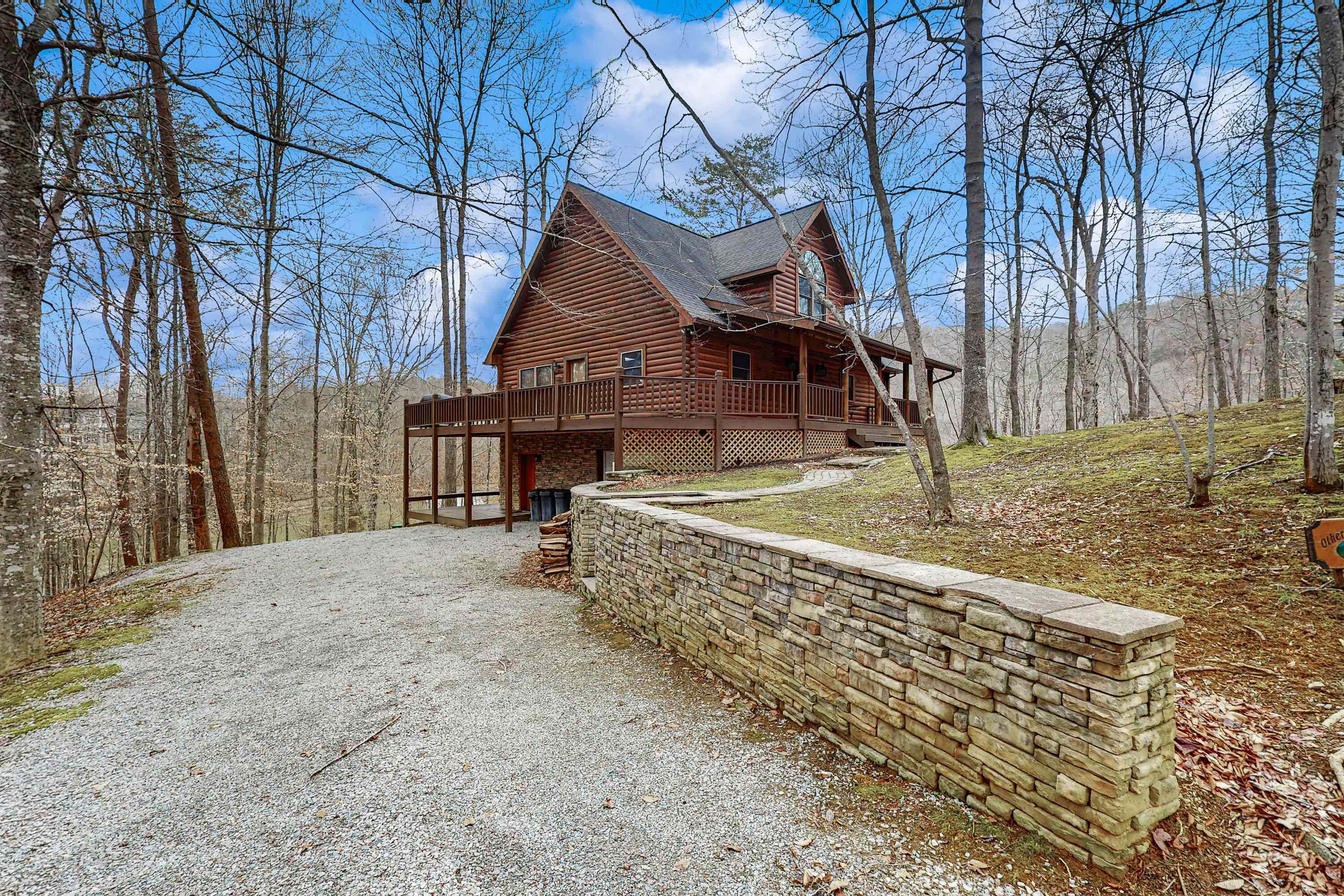 A log cabin with a deck and a stone wall in front.