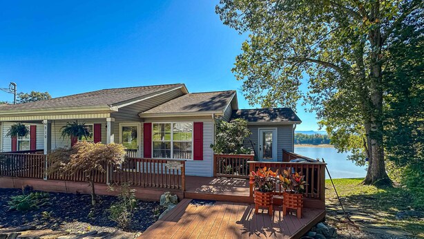 Une maison située au bord de l’eau, dotée d’une terrasse en bois, de plantes en pot et offrant une vue sur le lac.