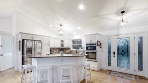 Une cuisine spacieuse avec des meubles blancs, un grand îlot central doté de tabourets et des appareils électroménagers modernes.