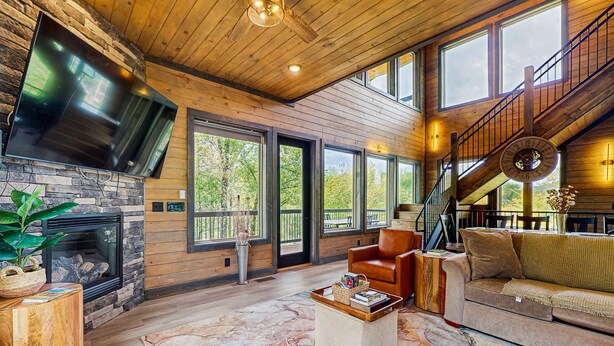 Un salón espacioso con chimenea de piedra, ventanas amplias, techo de madera y una escalera.