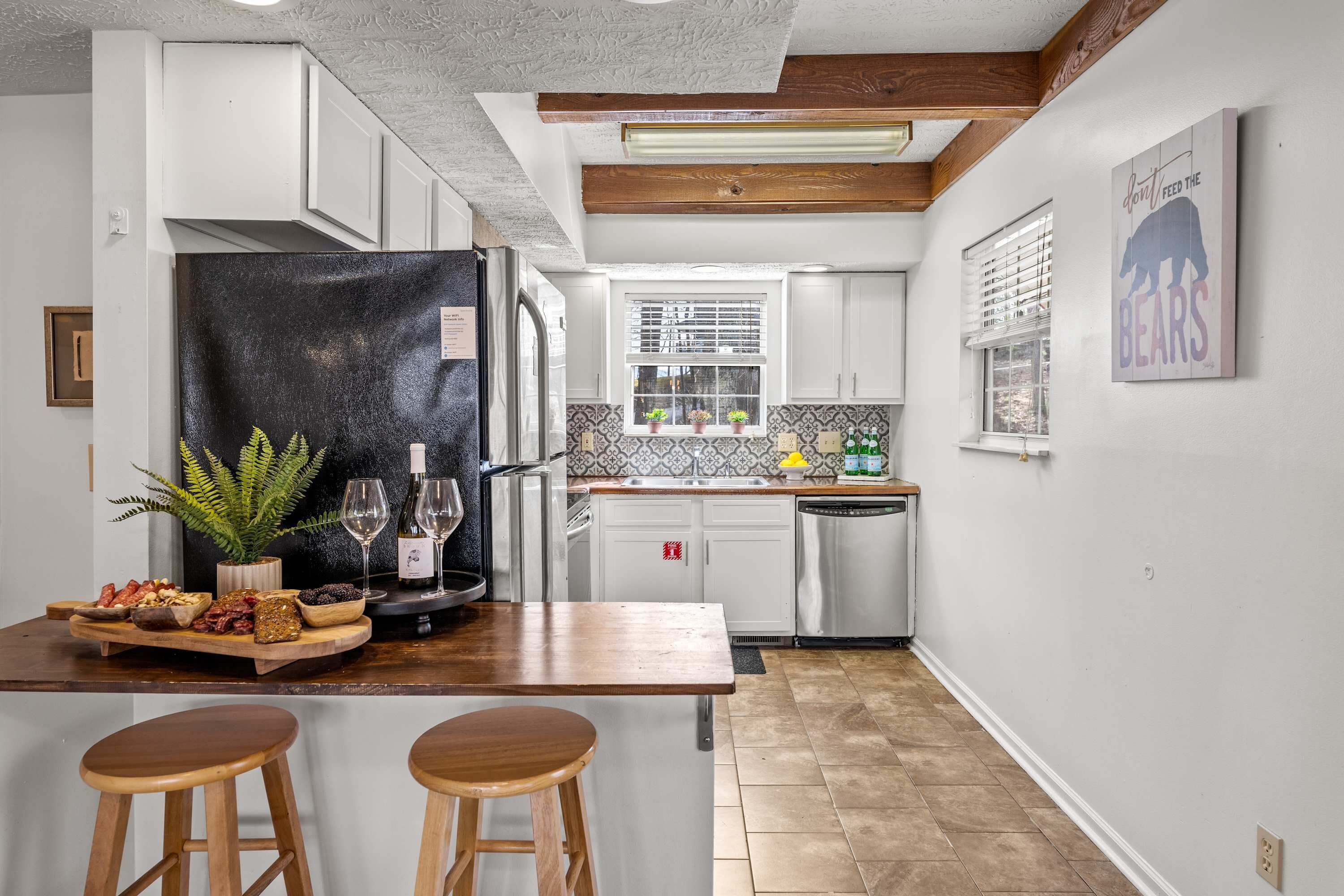 Una cocina con una isla de madera, taburetes de bar, un refrigerador y una ventana con persianas.