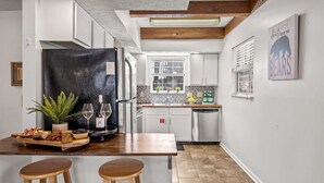 Eine Küche mit einer Holzeile, Barhocker, einem Kühlschrank und einem Fenster mit Jalousien.