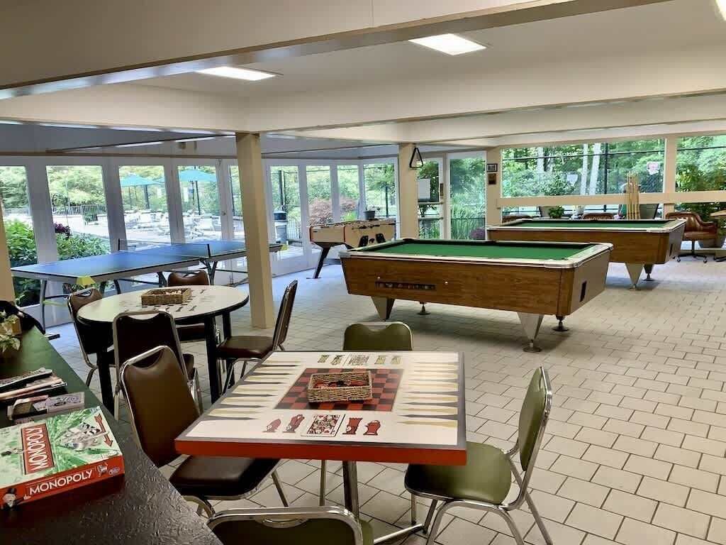 Una sala de billar con mesas y sillas, una mesa de billar y vistas al exterior.