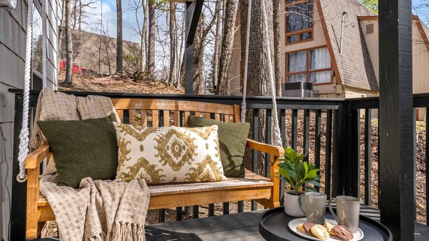 Eine Holzterrasse mit einer Bank, einem kleinen Tisch mit Keksen und zwei Tassen sowie einem Blumentopf.