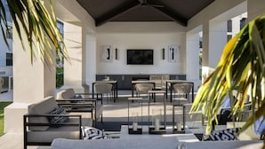 An outdoor patio with a flat-screen TV, seating area, and a kitchen counter. - Landing | Stunning 2BD, Pool, Clubhouse (Miromar Lakes)