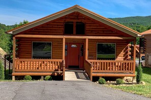 A wooden cabin with a red door, two front porches with benches, and a staircase leading to the upper level. - Serene & Spacious Log Cabin・Hot Tub・Screened Porch (Gatlinburg)