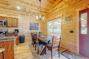 A cabin interior with a wooden interior, a dining table with chairs, a kitchen area with appliances, and a window with a view of the outside. - Serene & Spacious Log Cabin・Hot Tub・Screened Porch (Gatlinburg)
