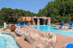 A swimming pool with a waterfall feature, lounge chairs, and a hot tub. - Serene & Spacious Log Cabin・Hot Tub・Screened Porch (Gatlinburg)