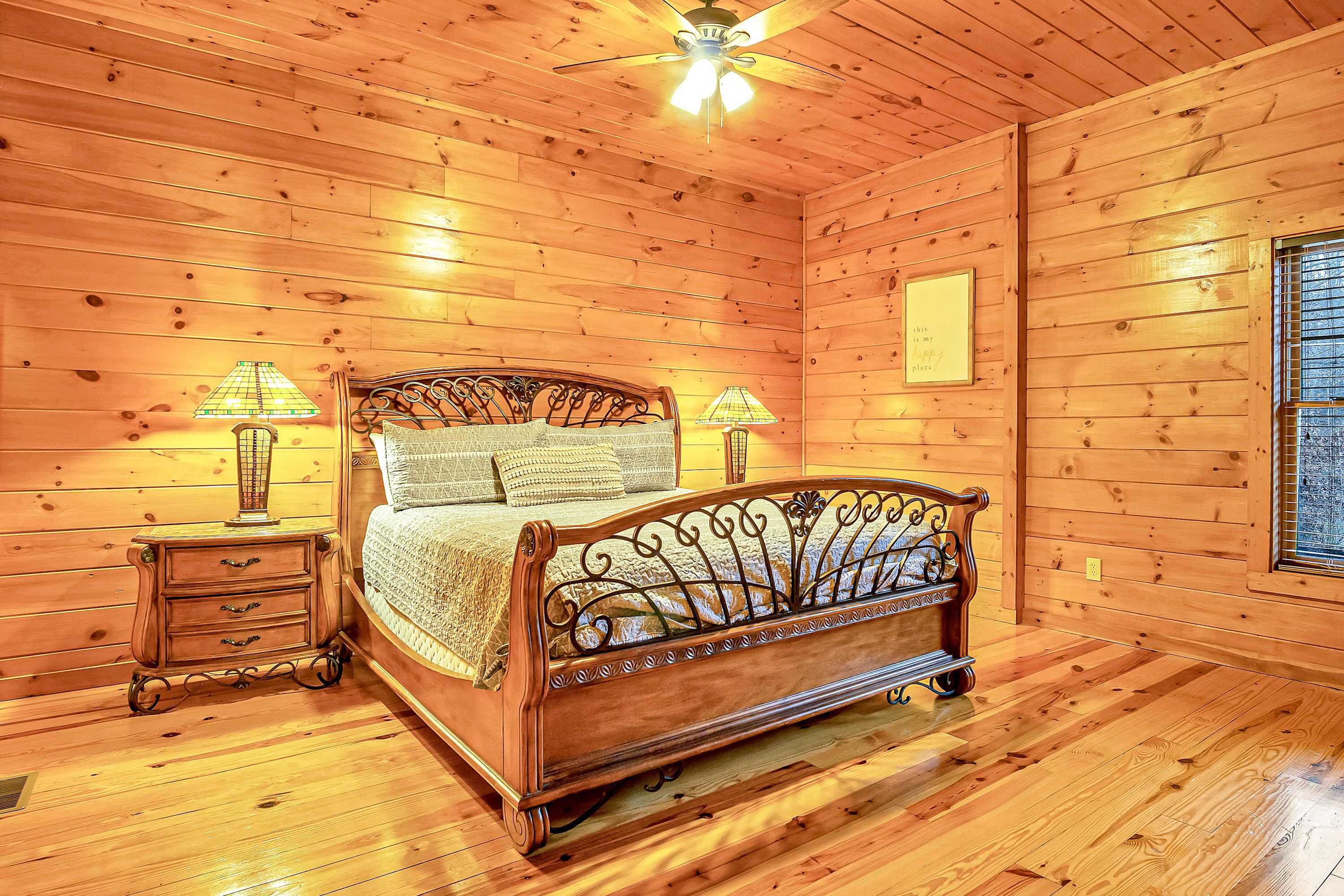 A wooden cabin bedroom with a bed, two nightstands, and a ceiling fan.