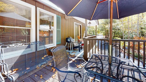 A covered outdoor seating area with metal chairs and a table, a large umbrella, and a wooden deck with a railing. - 1 Mi. from Downtown Gatlinburg・Games・River View (Gatlinburg)
