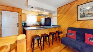 A compact kitchen with a central island, wooden walls, and a dark blue sofa with bear-themed cushions. - 1 Mi. from Downtown Gatlinburg・Games・River View (Gatlinburg)