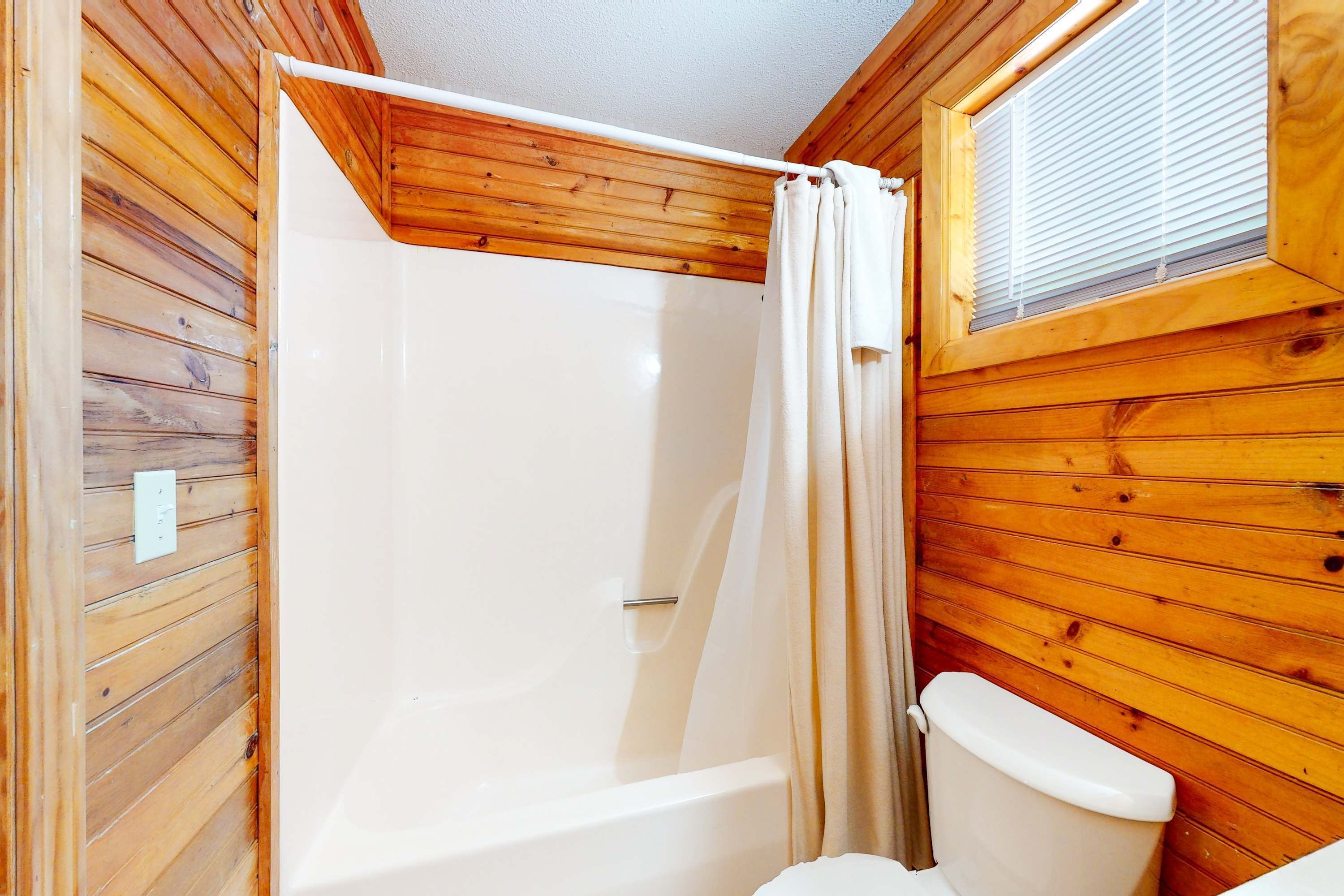 Baño de cabaña de madera con ducha, inodoro y ventana sobre el inodoro.