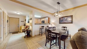 Un'area pranzo con un tavolo e sedie in legno, una cucina sullo sfondo e una porta che dà su un'altra stanza.