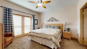 Una camera da letto con un letto, una ventola a soffitto, un comodino con una lampada, una sedia e una finestra con persiane.