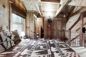 A rustic wooden interior with a patterned rug, a bed with a pillow, a staircase, and a door leading to another room. - Sevierville Smoky Mountain Cabin | Hot Tub & Views (Sevierville)
