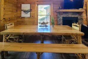 A wooden interior with a large table, benches, a stone fireplace, and a window with blinds. - Spacious Cabin, Sleeps 16, Games, Near Downtown (Pigeon Forge)