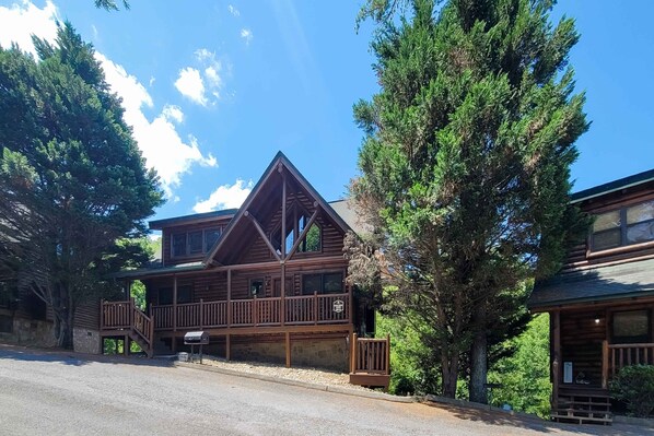 A two-story log cabin with a balcony, surrounded by tall trees. - Spacious Cabin, Sleeps 16, Games, Near Downtown (Pigeon Forge)