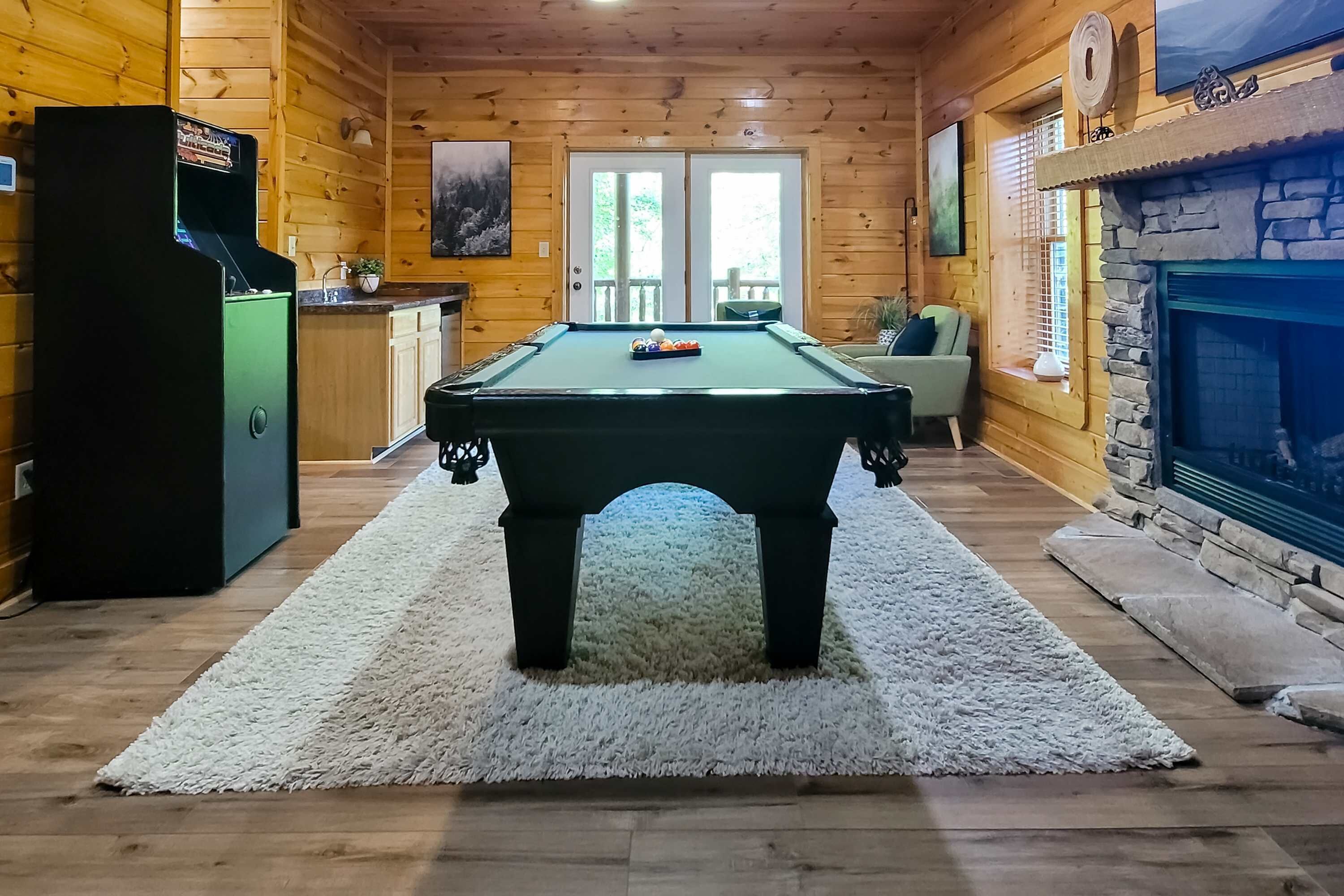 A pool table in a wooden cabin with a fireplace and a door leading outside.