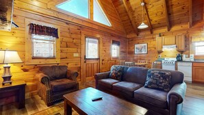 Een gezellig interieur van een chalet met houten wanden, een bank, een stoel, een tafel en een kitchenette.