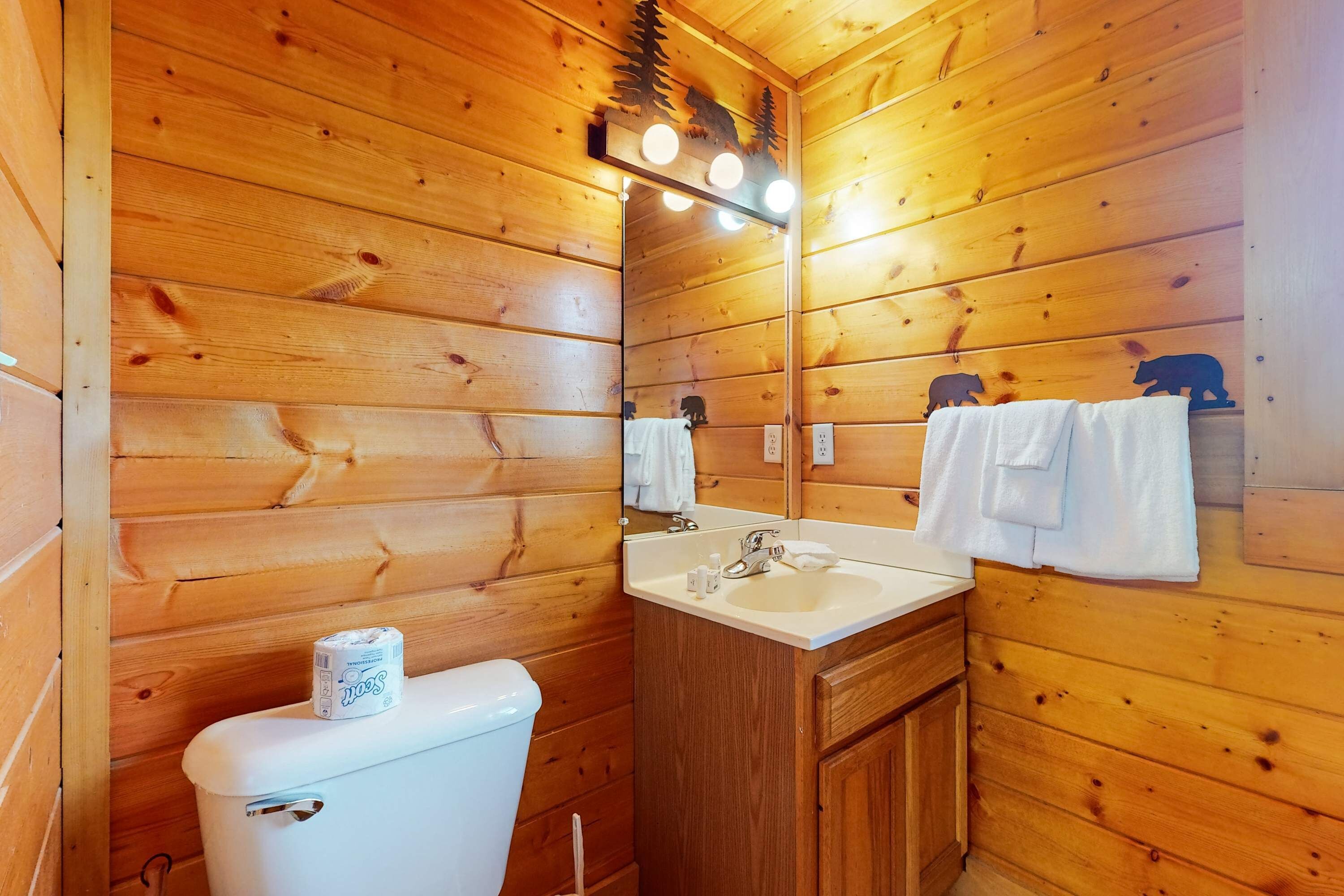 A wooden cabin bathroom with a toilet, sink, and mirror.