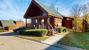 Een vakantiehuisje van hout met een veranda, een auto geparkeerd ervoor en een heldere lucht.