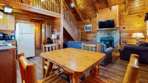 Een houten hut interieur met een eethoek, keuken, woonkamer en een open haard.