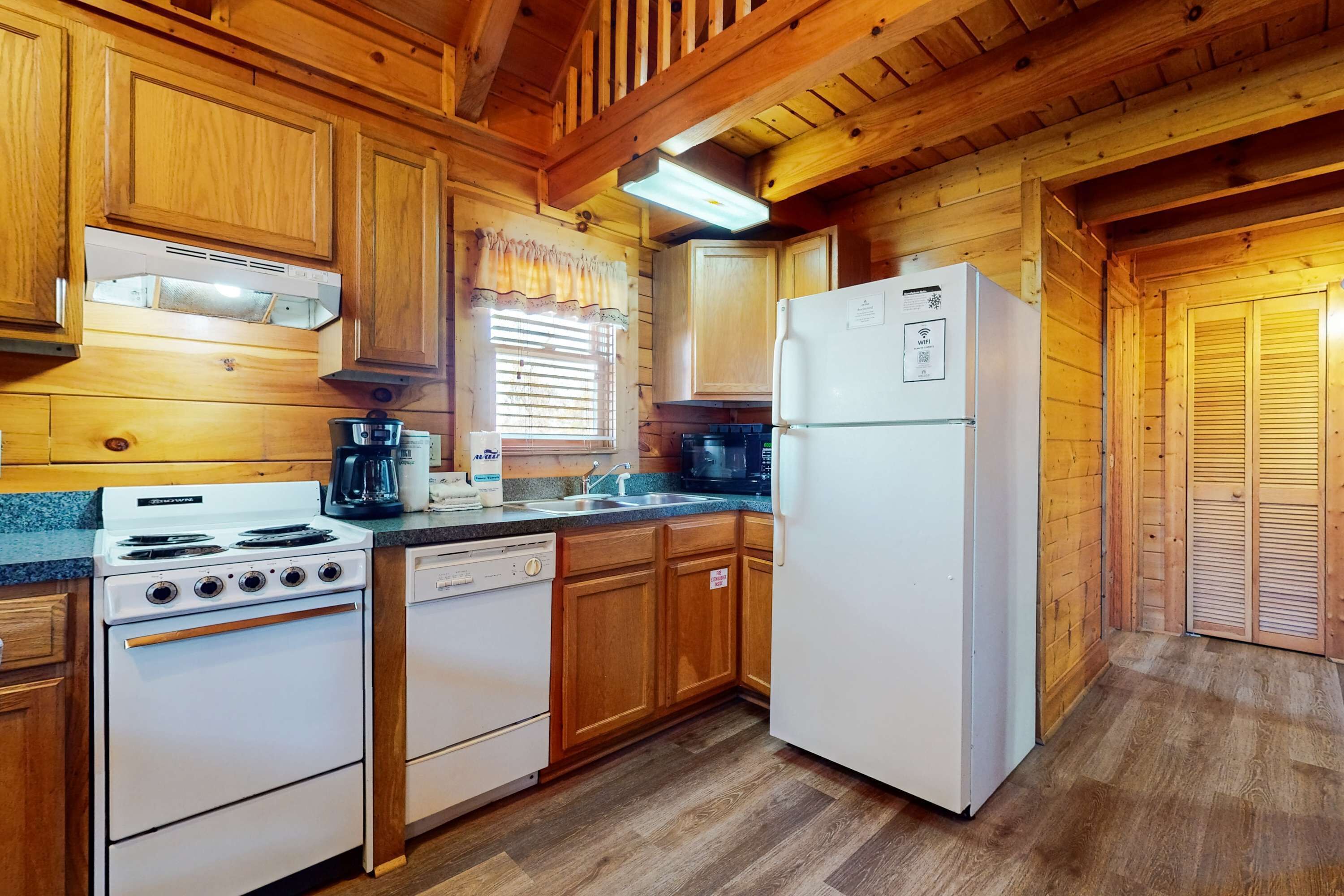 A wooden cabin-style kitchen with a stove, dishwasher, refrigerator, and wooden cabinets.
