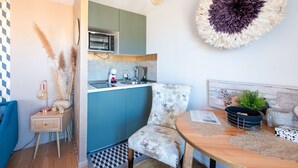 A modern kitchen with teal cabinets, a wooden dining table, and a decorative wall hanging. - L'Illusioniste studio vue mer dans le Suquet (Cannes)
