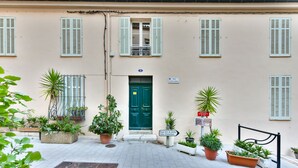 A building with a green door, multiple windows with shutters, and several potted plants. - L'Illusioniste studio vue mer dans le Suquet (Cannes)
