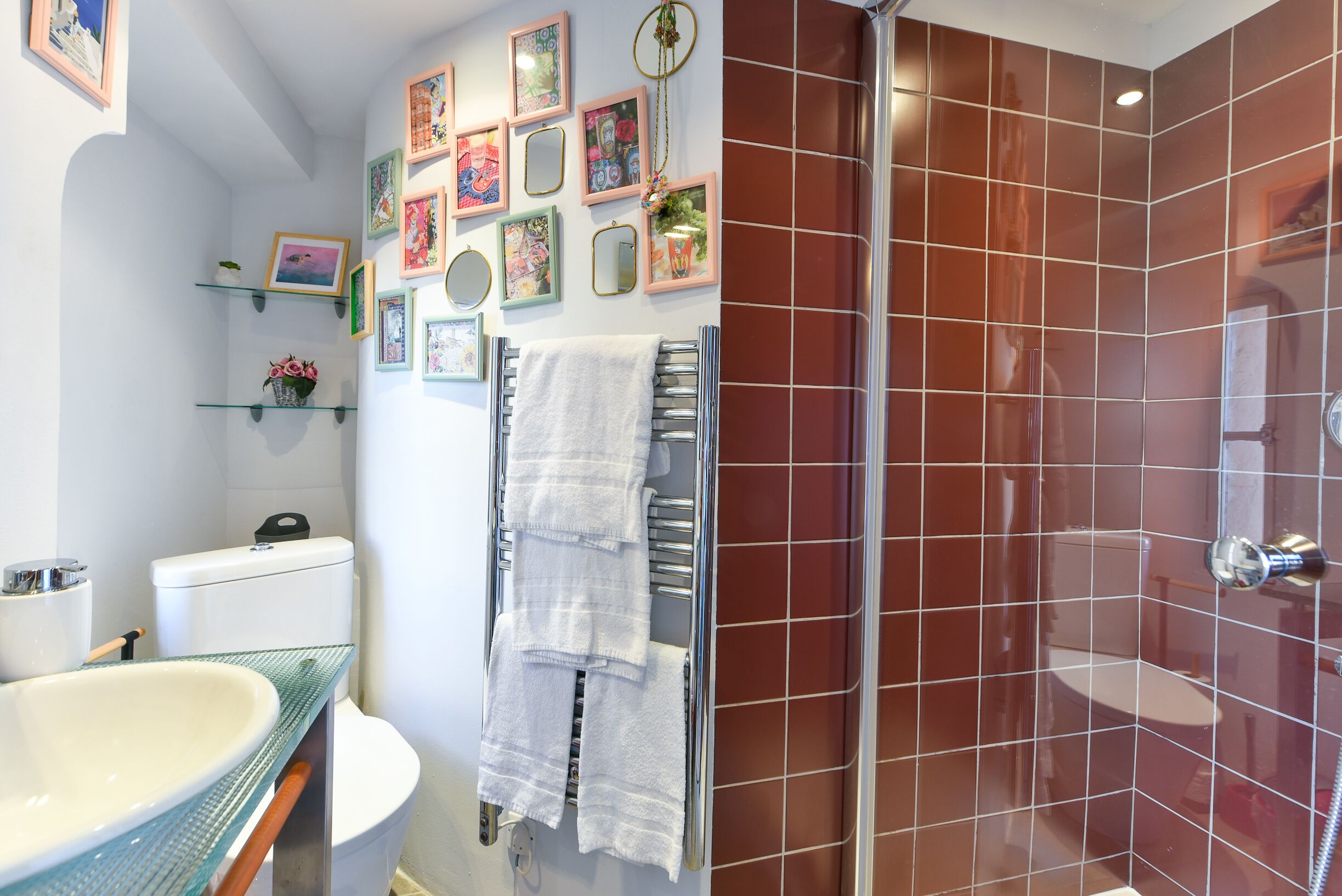 A bathroom with a glass shower enclosure, a white toilet, a glass sink, and a towel rack with multiple towels.