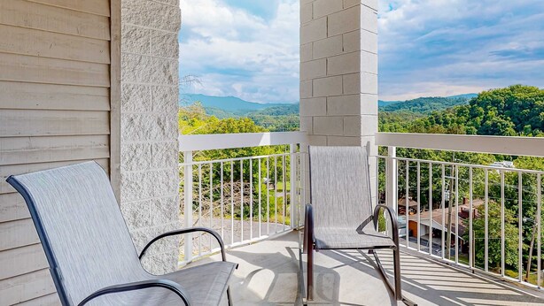 A balcony with two chairs, a white railing, and a view of green hills and buildings in the distance. - Mtn View Condo, Sleeps 8, Pool W Lazy River, Hot Tub (Pigeon Forge)
