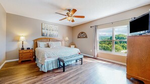 A bedroom with a bed, a bench, a ceiling fan, a TV, and a large window with a view. - Mtn View Condo, Sleeps 8, Pool W Lazy River, Hot Tub (Pigeon Forge)
