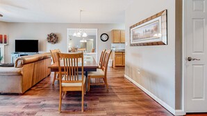 A modern living room with a wooden dining table and chairs, a leather sofa, and a flat-screen TV. - Mtn View Condo, Sleeps 8, Pool W Lazy River, Hot Tub (Pigeon Forge)