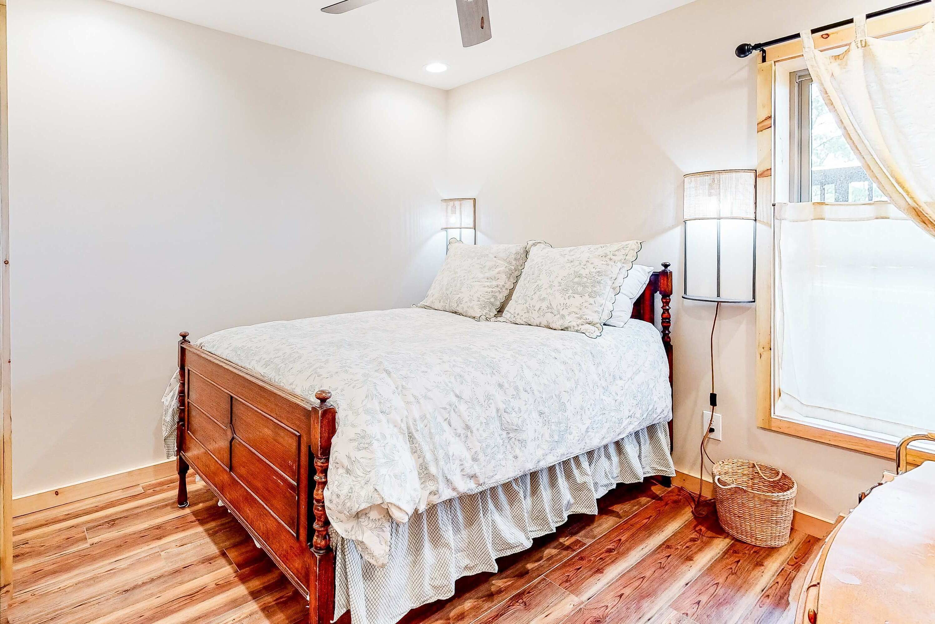 Quarto com cama de madeira, paredes brancas e janela com cortinas.