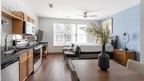 A compact living space with a kitchenette, a dining area, a bed, and a large window. - Landing | Amazing Studio, Pool, Gym (Birmingham)