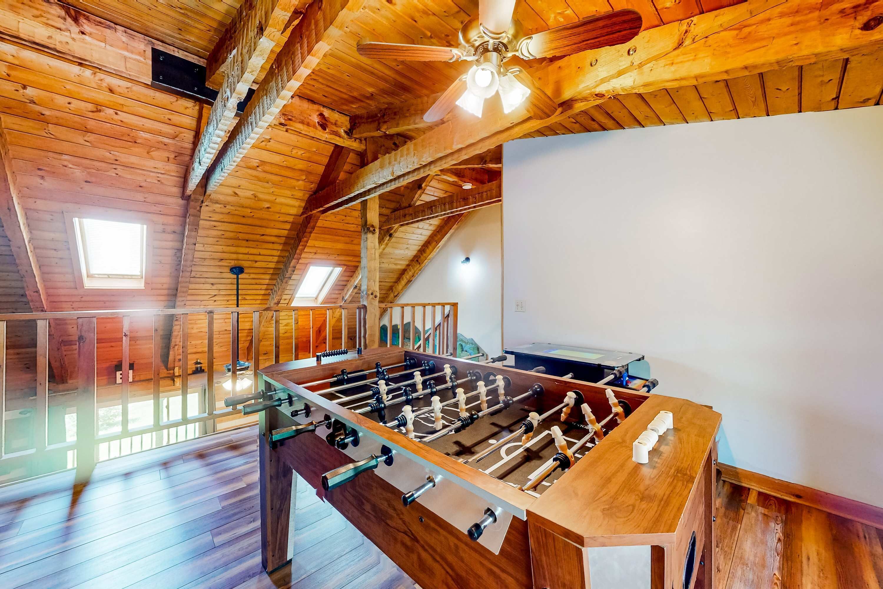 A wooden-floored room with a foosball table, a ceiling fan, and a staircase leading to an upper level.